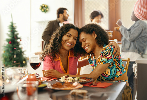 Smiling friends hugging and enjoy time spent together sitting at festive table during home party