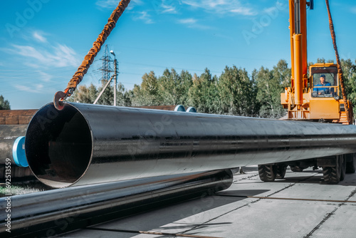 Unloading metal pipes for gasification in warehouse on summer day. Tractor unloads large diameter pipes.
