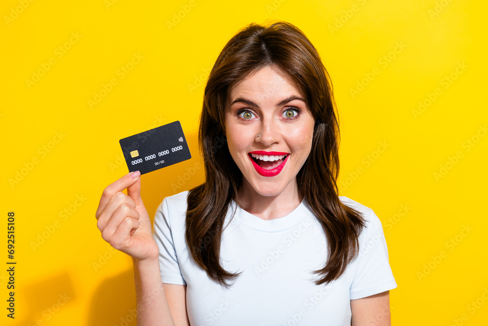 Photo of impressed adorable woman with brunette hair dressed white t-shirt presenting debit card isolated on yellow color background Photo of impressed adorable woman with brunette hair dressed white t-shirt presenting debit card isolated on yellow color background