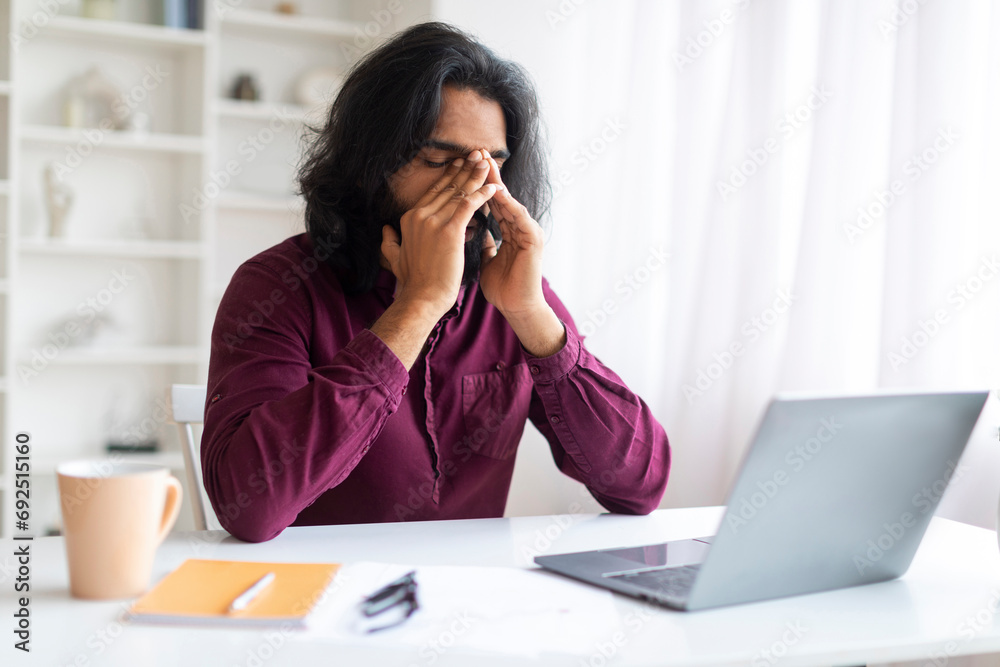Overworking. Tired Indian Man Suffering Headache While Working On Laptop At Home Overworking. Tired Indian Man Suffering Headache While Working On Laptop At Home