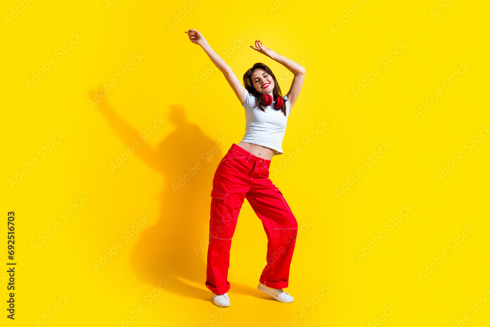 Full length photo of adorable positive lady wear white t-shirt earphones having disco fun isolated yellow color background Full length photo of adorable positive lady wear white t-shirt earphones having disco fun isolated yellow color background
