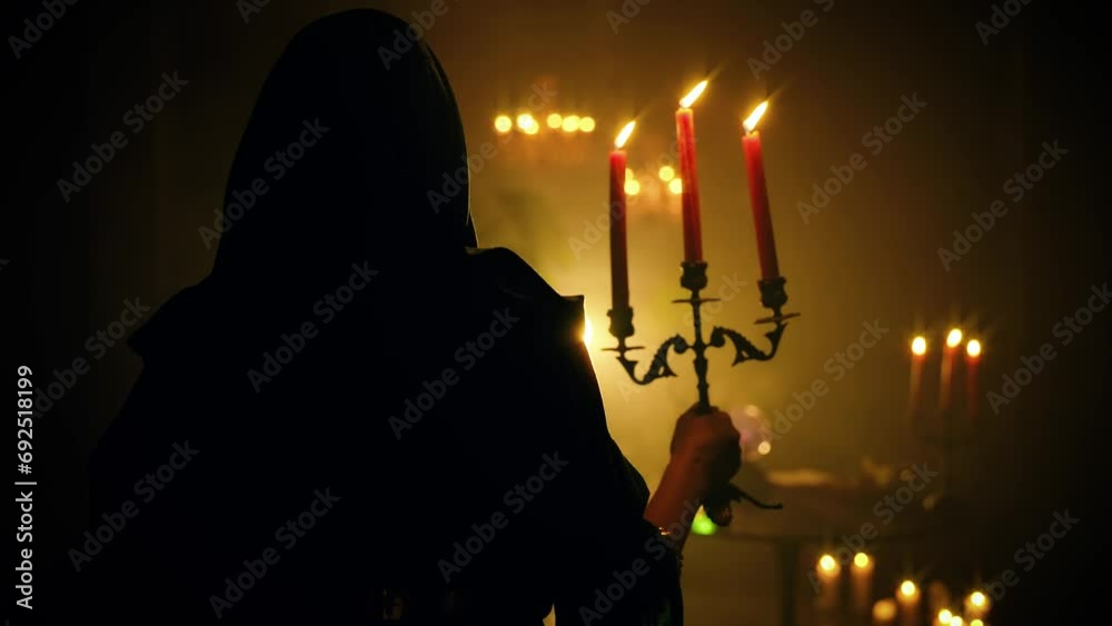 fantasy woman vampire in dark room holding old candlestick in hands candles burning warm light. Vintage style green cape dress with hood on head. Sexy girl back rear view. night black castle art. 4k
