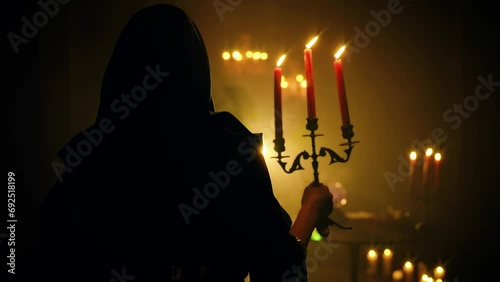 fantasy woman vampire in dark room holding old candlestick in hands candles burning warm light. Vintage style green cape dress with hood on head. Sexy girl back rear view. night black castle art. 4k photo