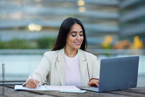Latin entrepreneur woman sitting with laptop computer taking notes outdoor Free Download Latin entrepreneur woman sitting with laptop computer taking notes outdoor - GFXLoad