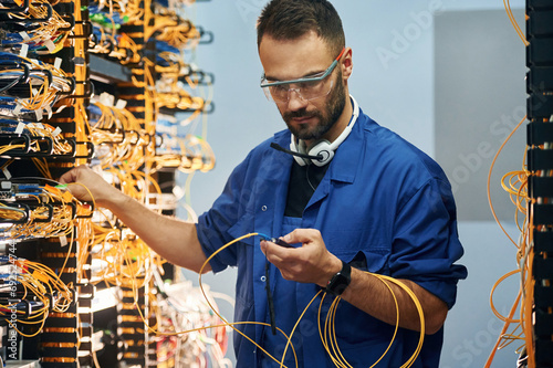 Modern technology routing. Young man is working with internet equipment and wires in server room