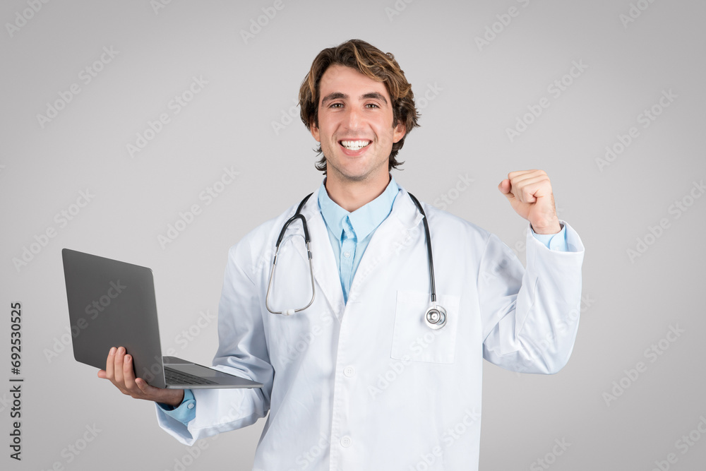 Excited caucasian doctor man working on computer with medical documents, got good news and clenching fist Excited caucasian doctor man working on computer with medical documents, got good news and clenching fist