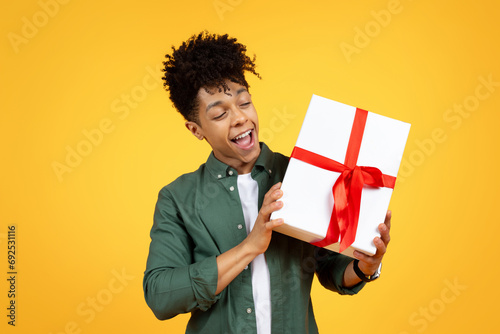 Positive black guy holding gift box, yellow background photo