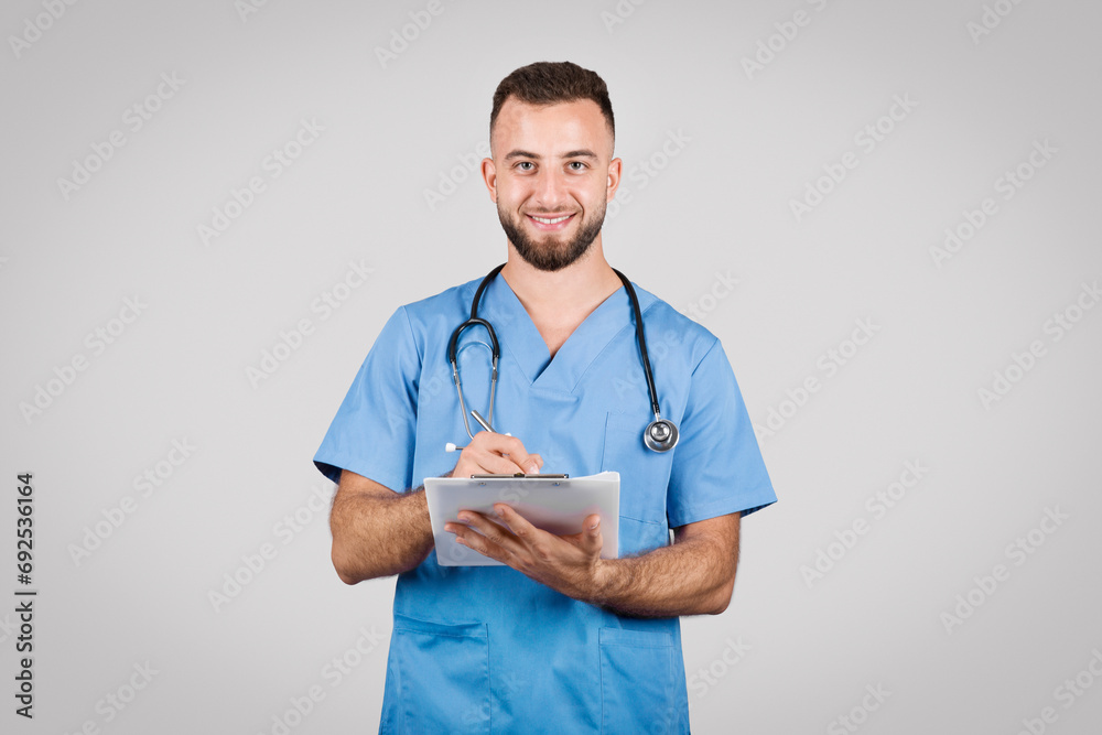 Smiling nurse writing on a clipboard in blue scrubs Smiling nurse writing on a clipboard in blue scrubs