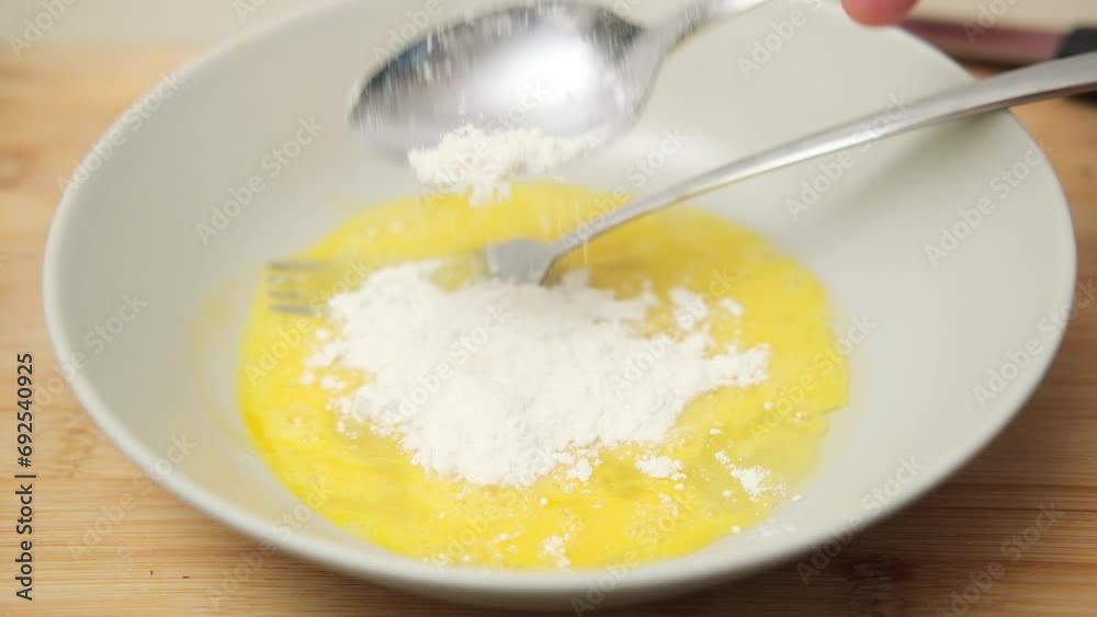 Stirring a raw chicken egg in a plate with a fork and flour, preparing for cooking Stirring a raw chicken egg in a plate with a fork and flour, preparing for cooking
