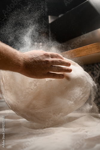 Baker's hands making a pizza dough in a flour on a table