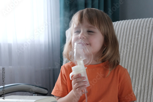 A little girl, a child of European appearance, blond hair, wearing an inhaler mask. Treatment of seasonal diseases with a nebulizer at home.