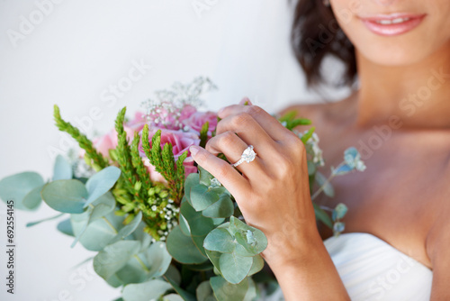 Diamond, wedding ring and hands of bride with bouquet, flowers and pride for commitment, celebration or marriage. Bridal, aesthetic and woman closeup with engagement jewelry or floral arrangement photo