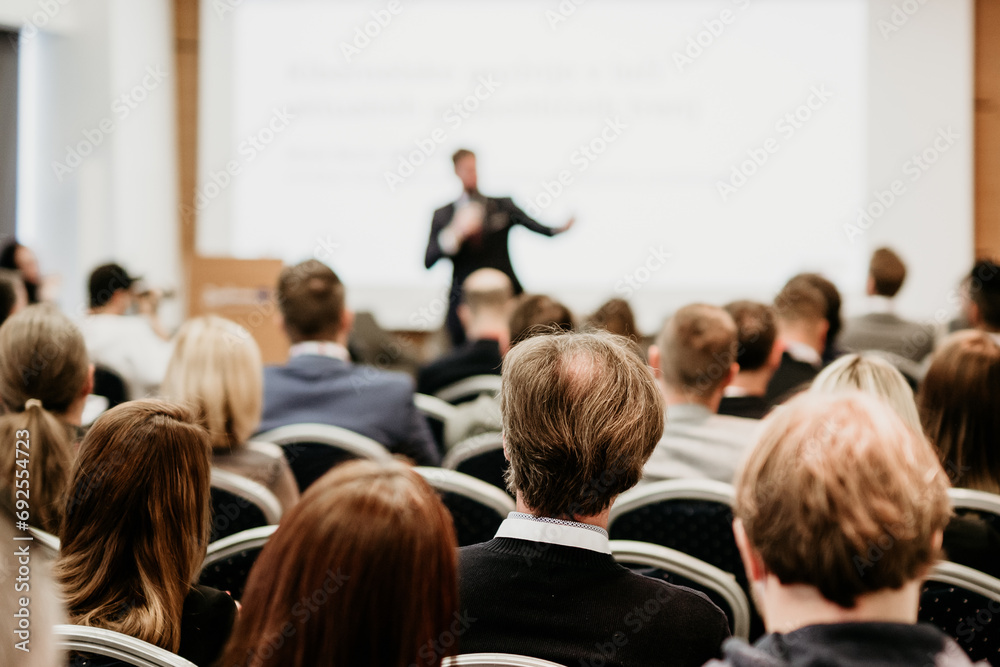 Speaker giving a talk in conference hall at business event. Rear view of unrecognizable people in audience at the conference hall. Business and entrepreneurship concept Speaker giving a talk in conference hall at business event. Rear view of unrecognizable people in audience at the conference hall. Business and entrepreneurship concept