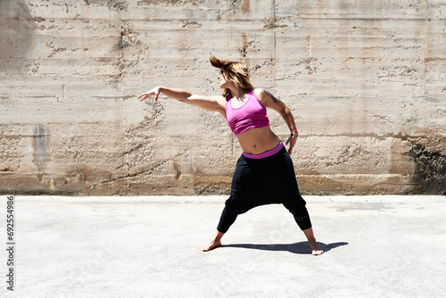 Active woman dancing against shabby wall on sunny day