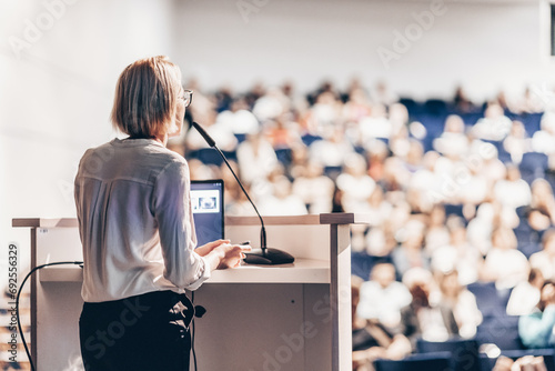 Female speaker giving a talk on corporate business conference. Unrecognizable people in audience at conference hall. Business and Entrepreneurship event