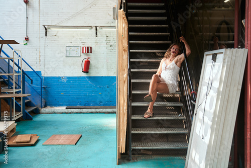 Longhaired womanlike guy sitting at the stairs and posing at lady dress alone