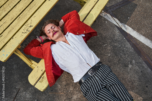 Street portrait of young womanlike man in trendy clothes laying with closed eyes
