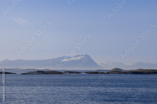 A captivating summer panorama taken from a ferry heading towards Lofoten Island  Norway  featuring the peaceful North Sea and serrated mountains crowned with snow  set against a radian sky