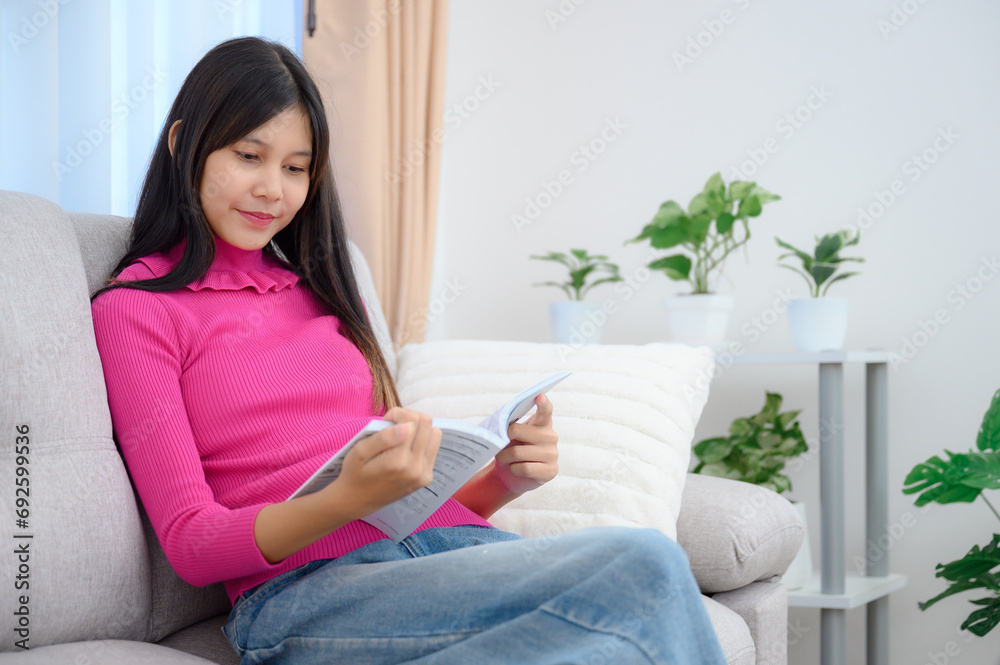 Asian teenage girl Reading a book at her home on the cloth sofa in the living room with a nice holiday at home. Asian teenage girl Reading a book at her home on the cloth sofa in the living room with a nice holiday at home.