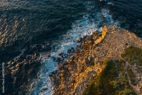 Drone top down view of ocean waves break on rocky headland, Portugal