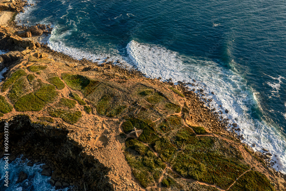 Ocean waves break on rocky island shores at sunset, drone shot