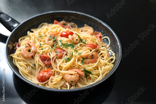 Spaghetti with shrimps, tomatoes and herbs a black frying pan on the stove top, cooking a Mediterranean seafood meal, copy space, selected focus