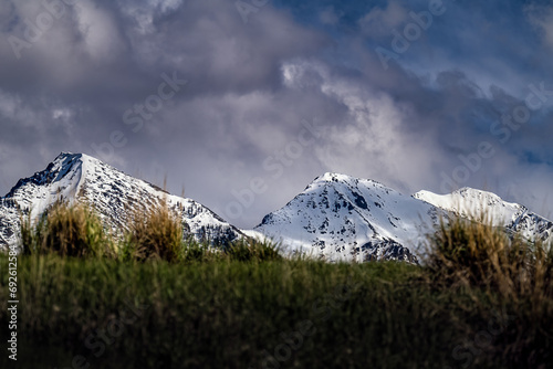 2023-12-23 SNOW COVERED MOUNTAINS OF THE ABSAROKA MOUNTAIN RANGE PEAKING OVER A VERY BLURRY GRASS MOUND WITH A DARK SKY IN PRAY MONTANA photo