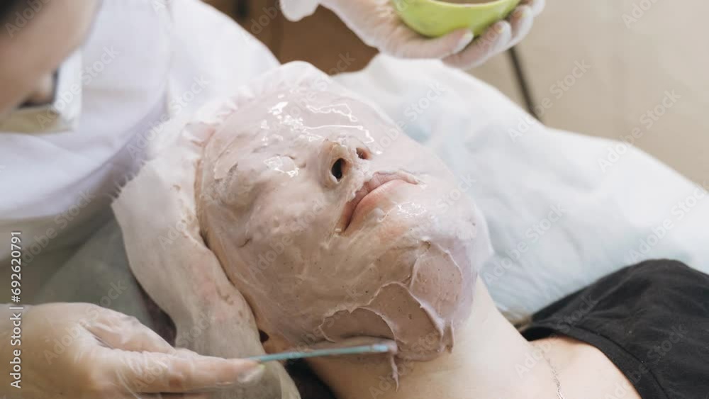 A cosmetologist applies an alginate mask to a womans face with a cosmetic spatula. Close-up. A cosmetologist applies an alginate mask to a womans face with a cosmetic spatula. Close-up.