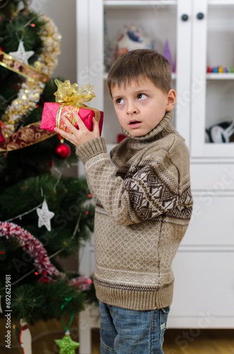 Cute boy put gift with a bow to his ear and guess what's in box
