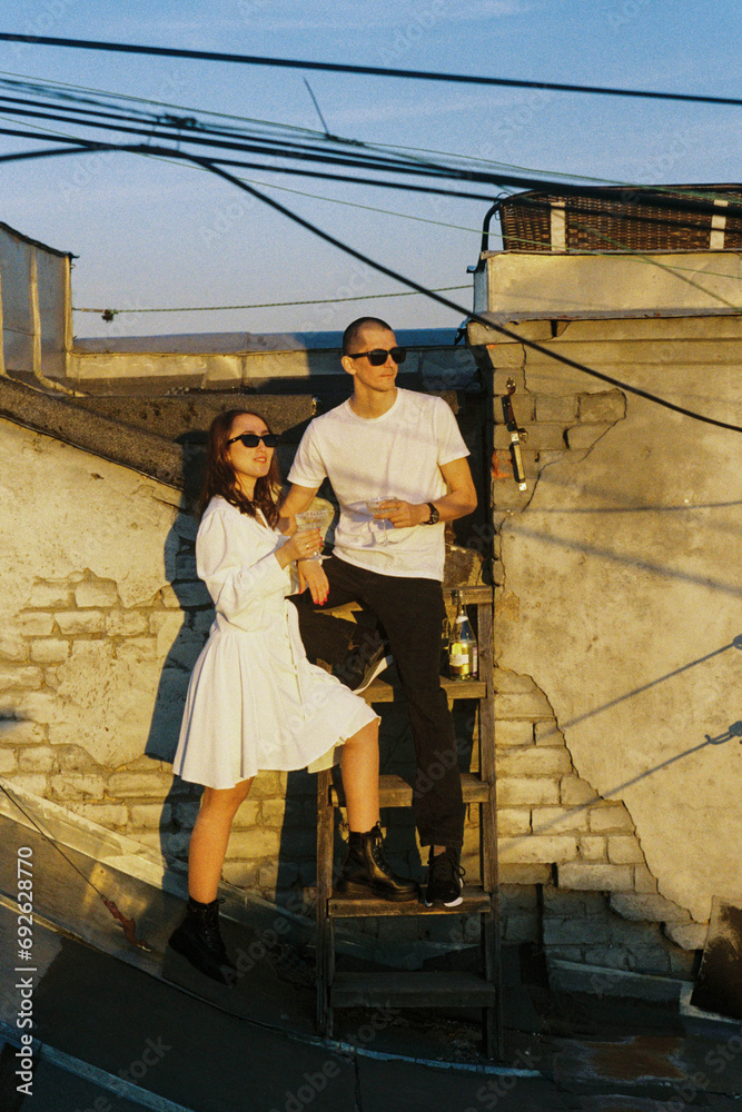 A man and woman standing on a ladder holding wine glasses on a roof.