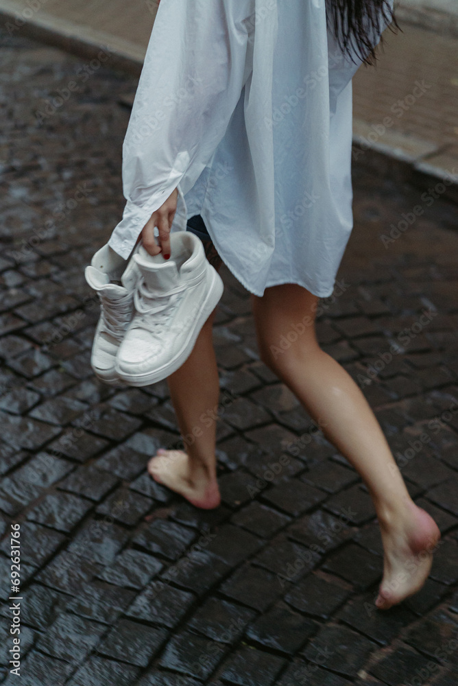 Woman walking down street in rainy weather in white shirt and blue jeans shorts Woman walking down street in rainy weather in white shirt and blue jeans shorts