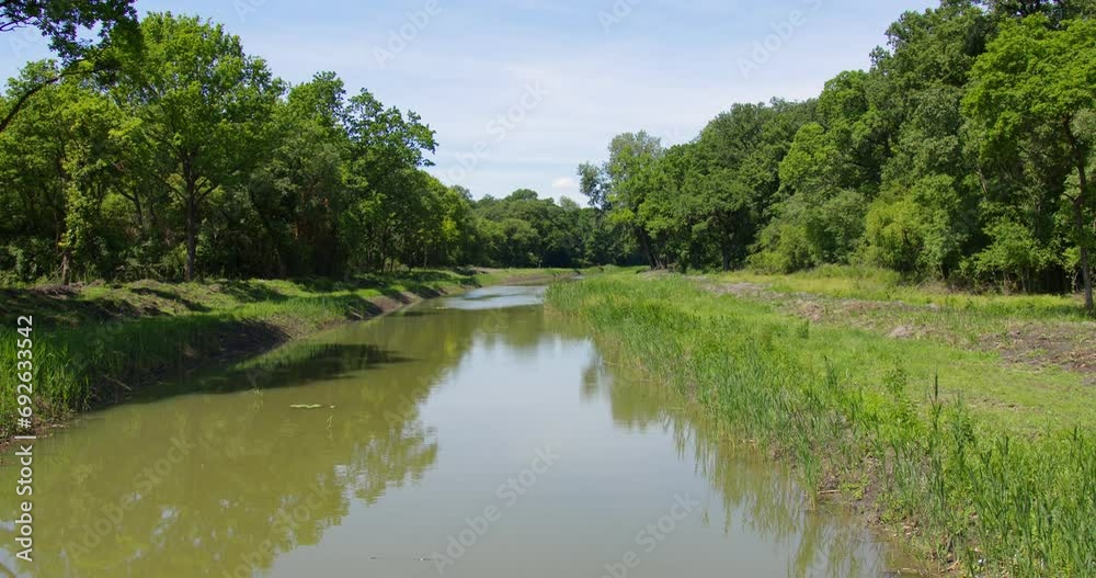 Still wide shot of a river flowing through wooded area in sunny spring day Still wide shot of a river flowing through wooded area in sunny spring day