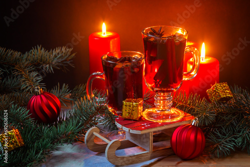 Glasses of mulled wine, burning candles, christmas balls, pine branches and gifts on wooden table. Selective focus.