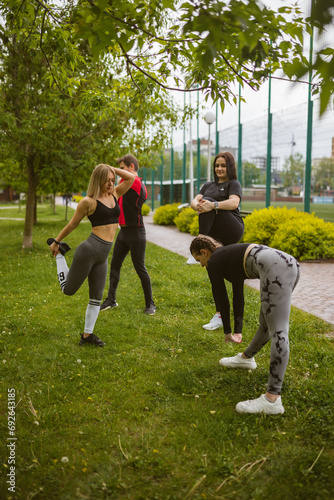Fototapeta Naklejka Na Ścianę i Meble -  Athletes in tracksuits warm up muscles before training on lawn grass. People group prepare to active workout in city garden