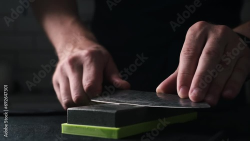 Male Hands Sharpening Kitchen Knife With Water Whetstone On A Kitchen Table, Close Up View photo