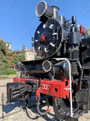 A steam-powered locomotive parked against the backdrop of urban development.