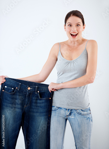 Surprise, weight loss and woman with jeans, change in size and white background in studio. Wow, shocked and portrait of person with crazy reaction to transformation in fitness or large denim pants