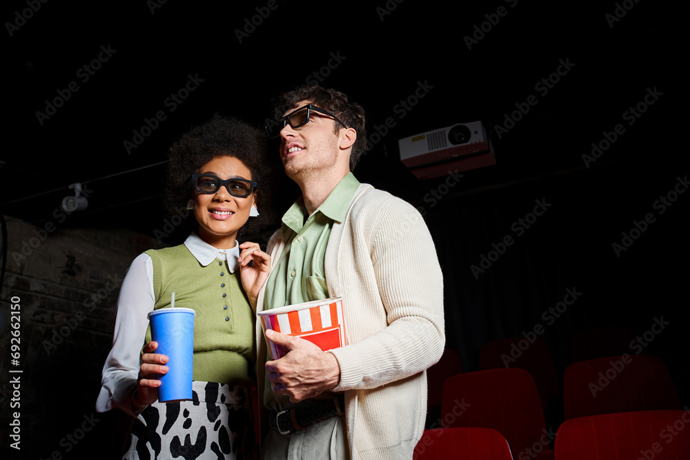 jolly multiethnic couple in 3d glasses holding soft drink and popcorn while on their date at cinema jolly multiethnic couple in 3d glasses holding soft drink and popcorn while on their date at cinema