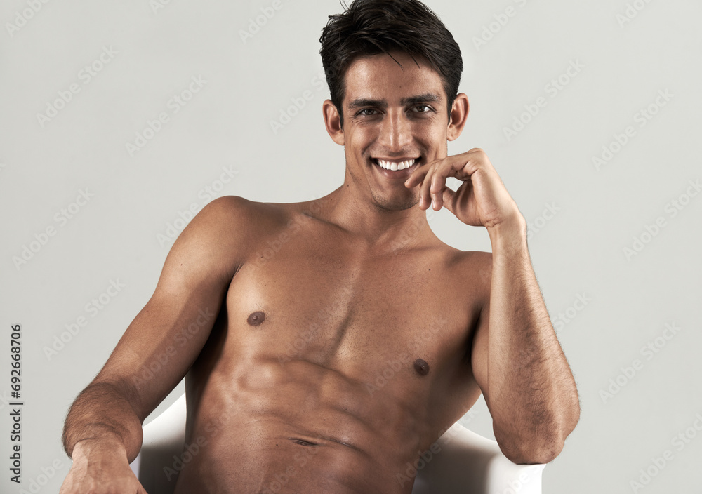Fototapeta premium Muscular, man and shirtless portrait in chair to relax in white background of studio. Happy, model and person with a smile for wellness, confidence and bodybuilder with a six pack from fitness