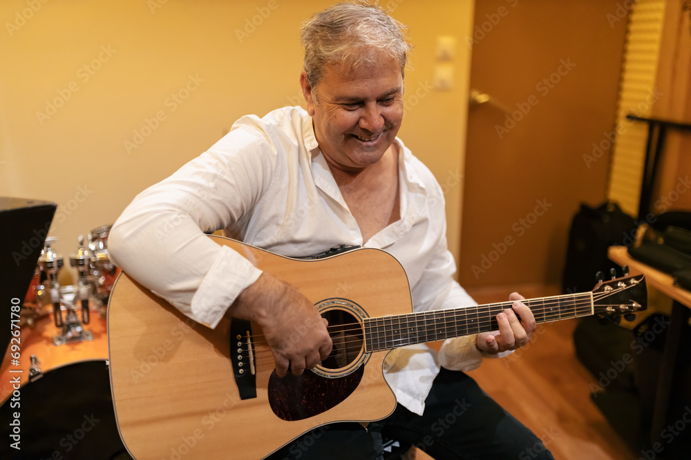 Obraz premium Positive mature man playing acoustic guitar in studio