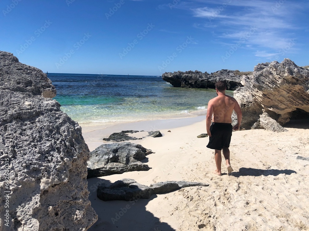 a man standing on a beach facing the ocean water and rocks, Rottnest island, Australia
