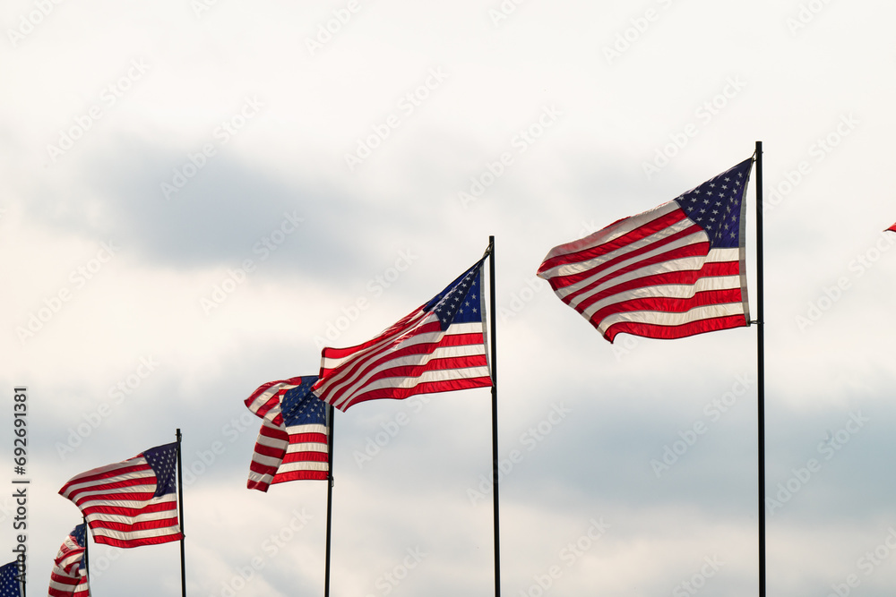 Four United States American Flags flying in front of a blue sky in a horizontal line patriotic display fall leaves