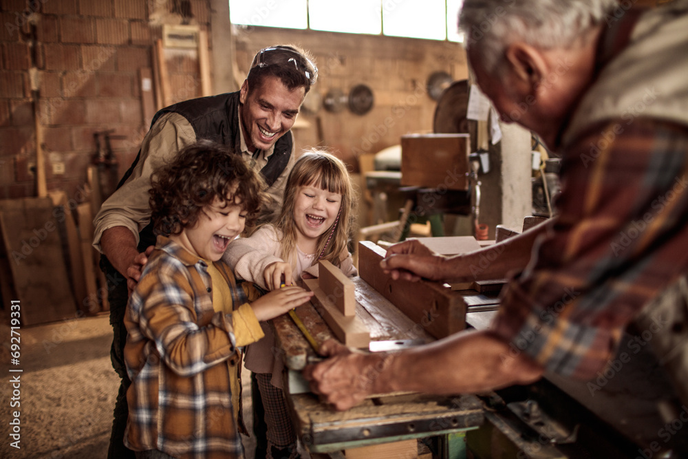 Cute little children working with older carpenters in workshop - obrazy, fototapety, plakaty 