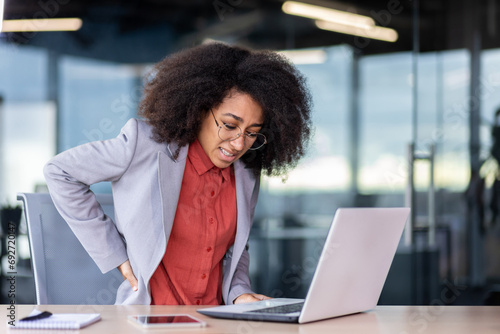 Female office worker suffers from back pain, holds her hand on her lower back, posture problems, pinched nerve from sitting work.