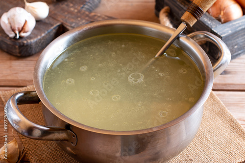 Saucepan with bouillon with a ladle on wooden table. Bone broth photo