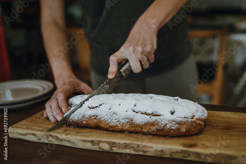 Women's hands cutting fruitcake on board with knife.