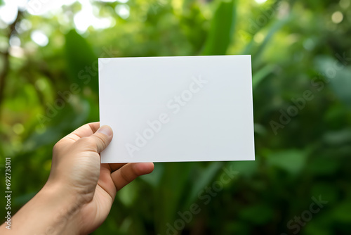 Hand holding a blank white card against a green foliage background