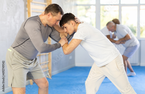 Adult man and young guy judokas practicing judo technique in gym..