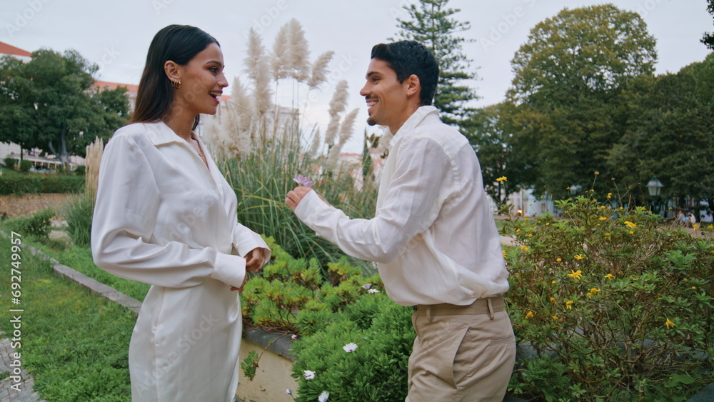 Stylish lovers walking garden. Latina gentle man putting flower behind woman ear Stylish lovers walking garden. Latina gentle man putting flower behind woman ear