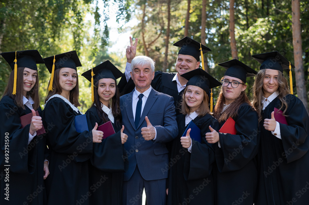 University professor and seven students rejoice at graduation and show thumbs up outdoors. 